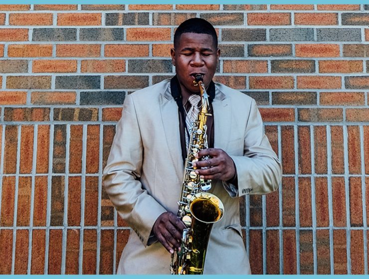 man playing tenor saxophone against a wall