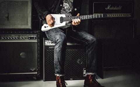 male guitarist sitting on amps playing