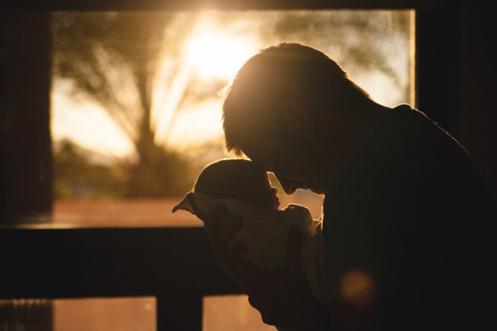 a man touching heads with his baby at sunset