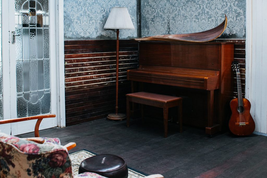 old piano in a room next to guitar and lamp