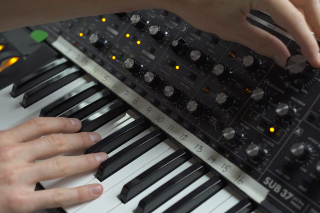 closeup of hands playing Moog SUB37 synthesizer